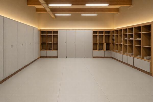 50mm重防撞软包在运动场馆更衣室墙面的全景，浅灰色平面款大面积铺设，暖色调灯光营造安全温馨氛围，展示板材在高频撞击区域的大面积防护效果